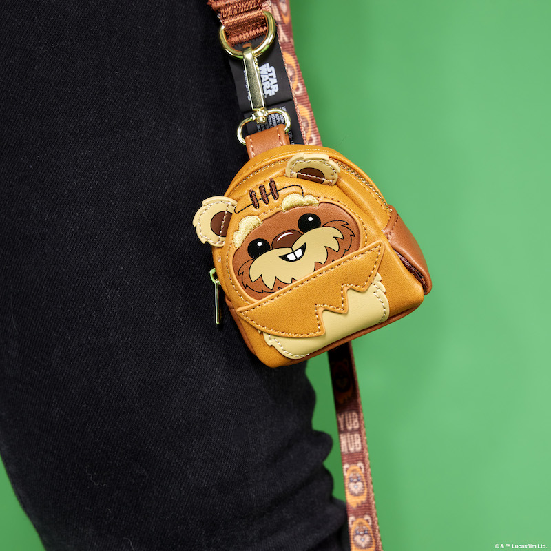Close up image of the Ewok Treat & Disposable Bag Holder, featuring a mini backpack shape with Star Wars Ewok details and 3D ears, resting against a black pant leg and a green background. 
